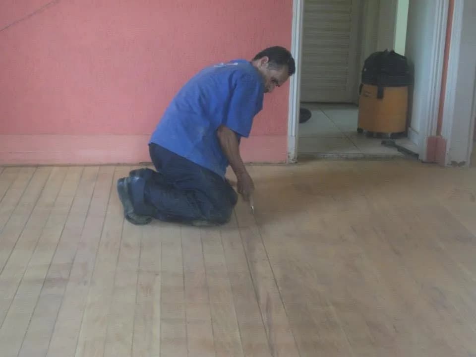 Profissional realizando raspagem de tacos de madeira ajoelhado no chão